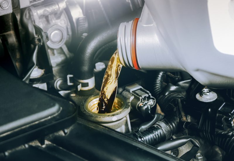 Close up of a bottle of motor oil being poured into a car combustion engine for lubricate. Oil change in car engine, Auto maintenance service concept.